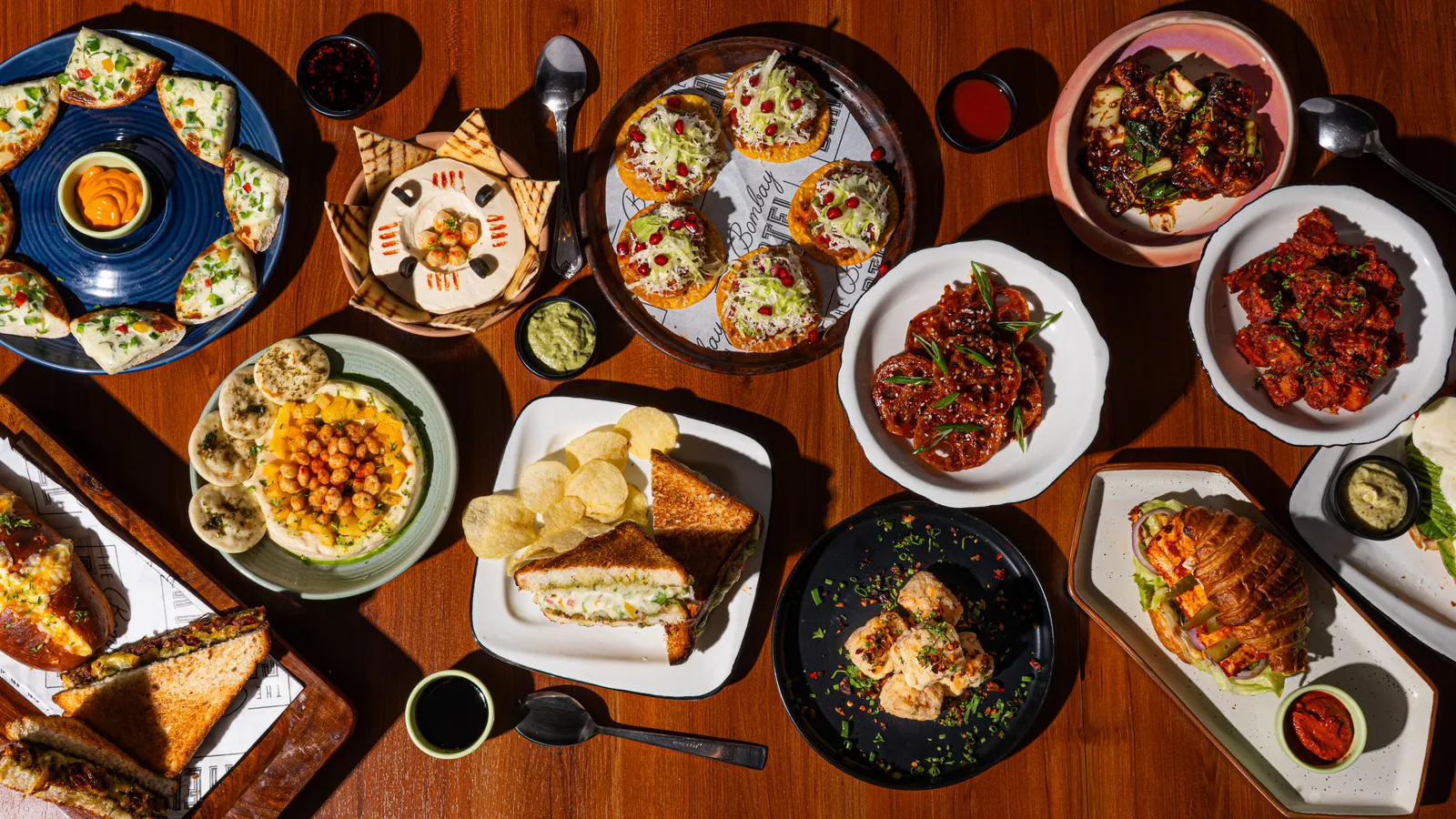 An overhead spread of shared plates, small bites and dips across a wooden table.
